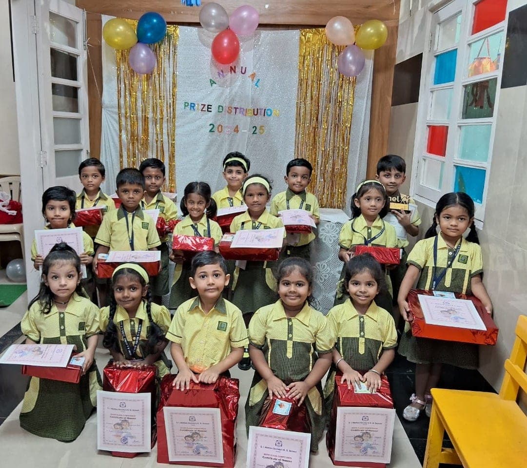 Sixteen Kindergarten children kneeling and standing with wrapped prizes and Inter Class Competition certificates of honour, in front of a gold and white prize-day backdrop.
