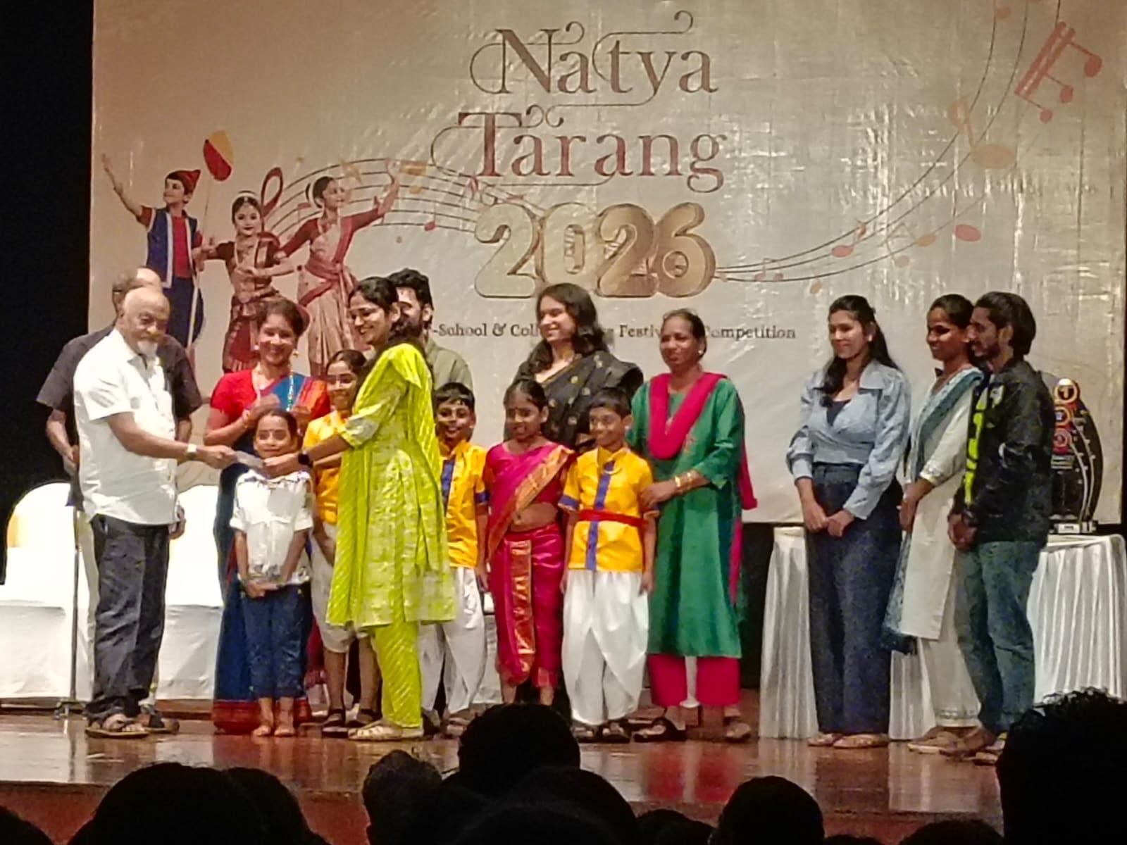 Children of the Primary Section in dance costume on the Natya Tarang 2026 stage with their teachers, as the group receives its prize for costume and props.