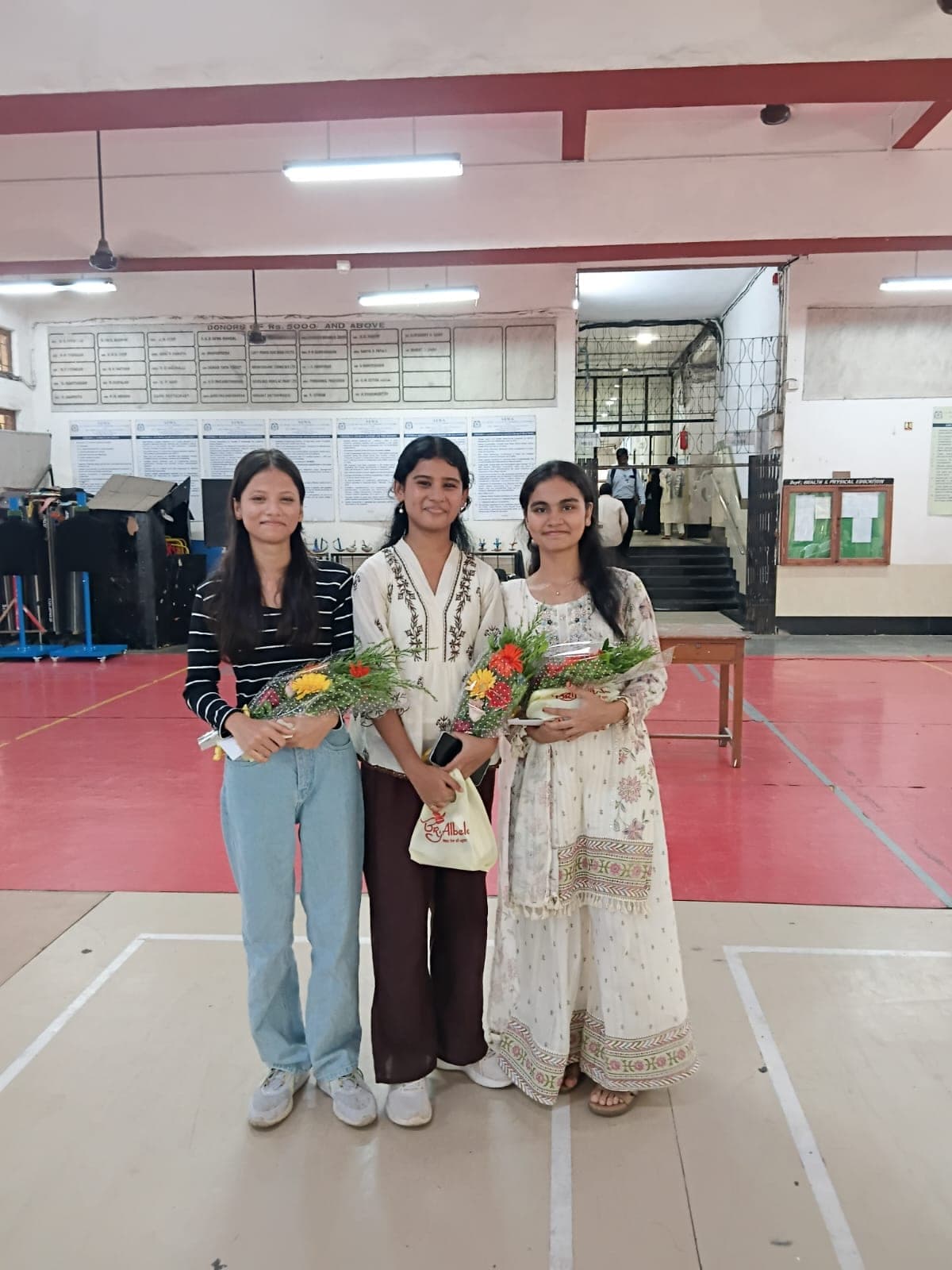 Three SIWS High School students standing together in the school hall, each holding a bouquet and an award after the 2026 SSC results.