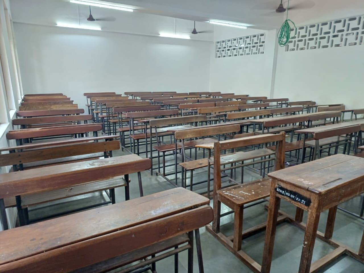 A Junior College lecture room with rows of wooden bench desks, ceiling fans and tube lights, empty between classes.