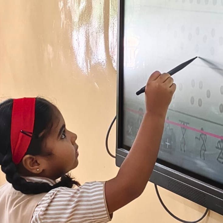 A young student in school uniform reaching up to draw on an interactive smart board with a stylus.