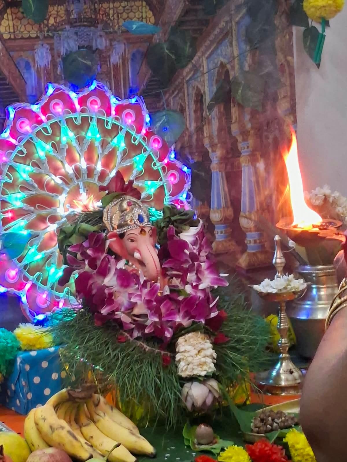 Close-up of the Ganesha idol garlanded with purple orchids and jasmine, set against a lit decoration, as the aarti lamp is offered.
