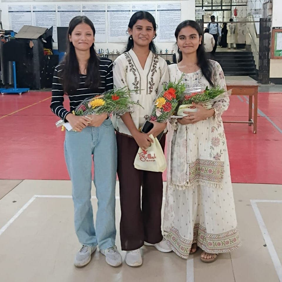 Three SIWS High School students standing together in the school hall, each holding a bouquet and an award after the 2026 SSC results.